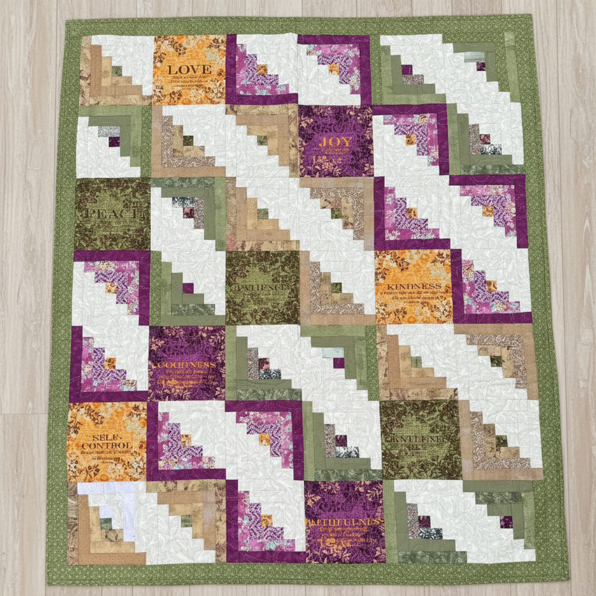 Handmade log cabin quilt with inspirational words like Love, Joy, Peace, Kindness, and Faithfulness in green, purple, gold, and cream tones.