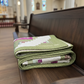 Folded green quilt with floral patterns on a wooden bench in a church setting