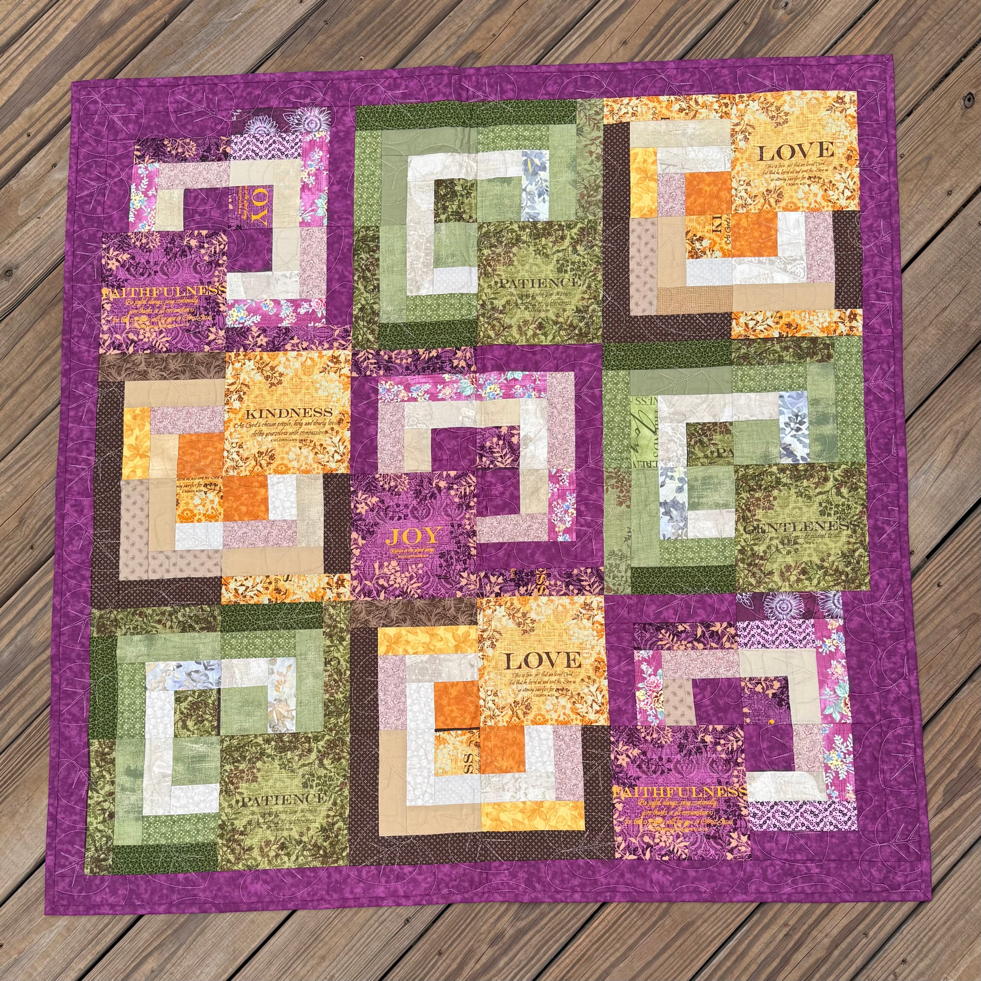 Handmade inspirational quilt with purple borders and colorful patchwork blocks featuring words like Love, Joy, Kindness, Patience, and Faithfulness.