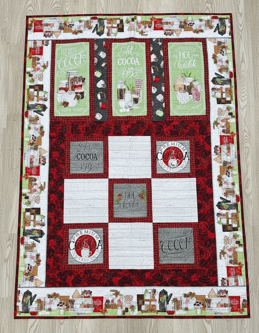 Handmade winter throw quilt with cocoa-themed panels, hot chocolate mugs, marshmallows, and festive red and green borders.
