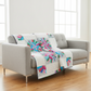 Colorful quilt draped over a gray sofa in a bright room with large windows.