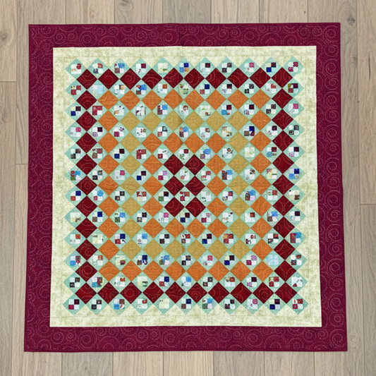 Handmade scrappy 4-patch quilt in brick red, orange, yellow, and green tones, shown flat with a classic patchwork layout