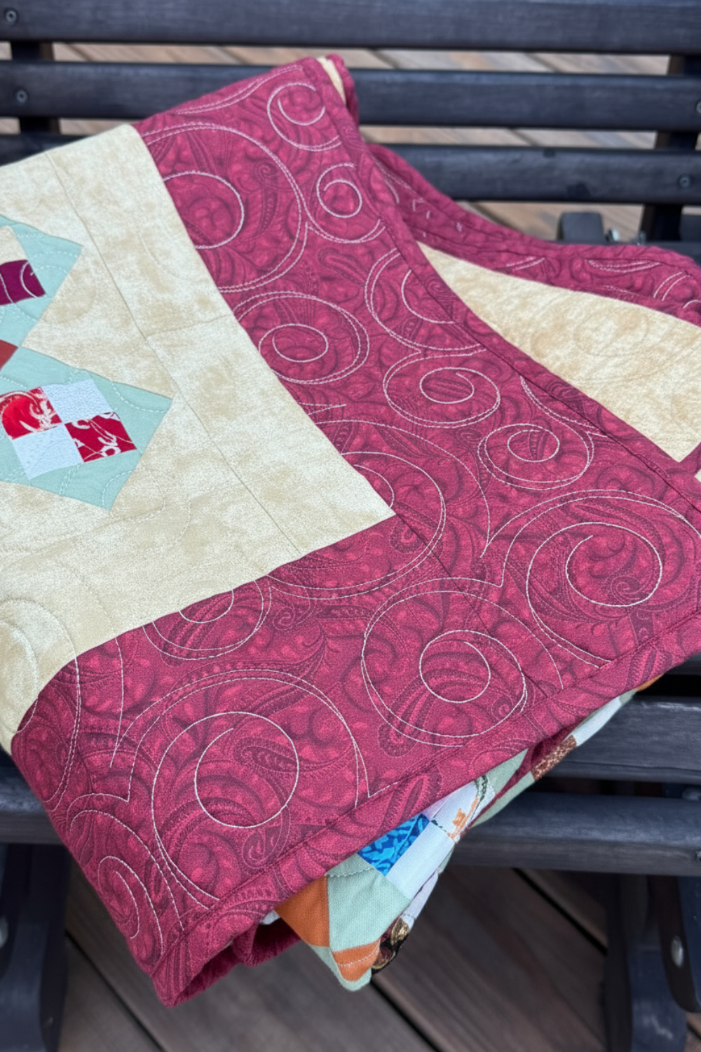 Folded scrappy 4-patch quilt displaying quilted texture and rich autumn colors on a wooden bench