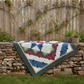 Classic Log Cabin Star quilt with a colorful pattern draped over a stone wall with a wooden fence and plants in the background.