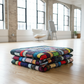 Folded stained glass quilt on a wooden floor with large windows in the background