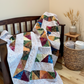 4‑Patch Charm quilt draped on a wooden bench indoors, displaying colorful patchwork fabric, quilting texture, and cozy scale.