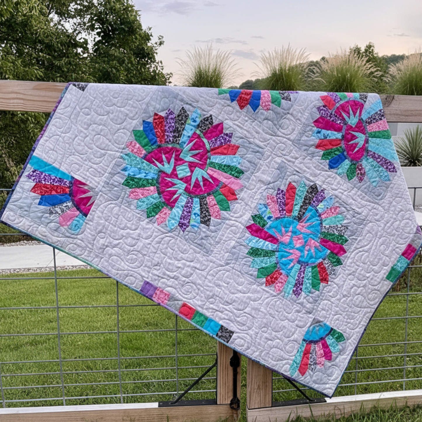 Colorful quilt with floral patterns draped over a wooden railing outdoors.