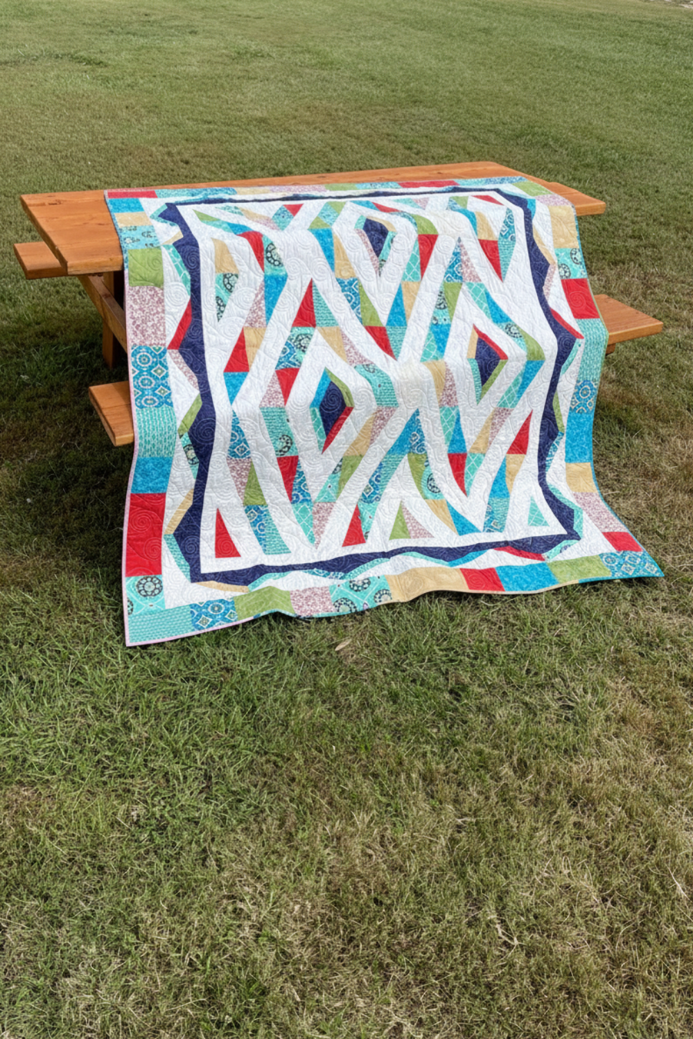 Prism quilt displayed as a throw over wooden picnic table outdoors