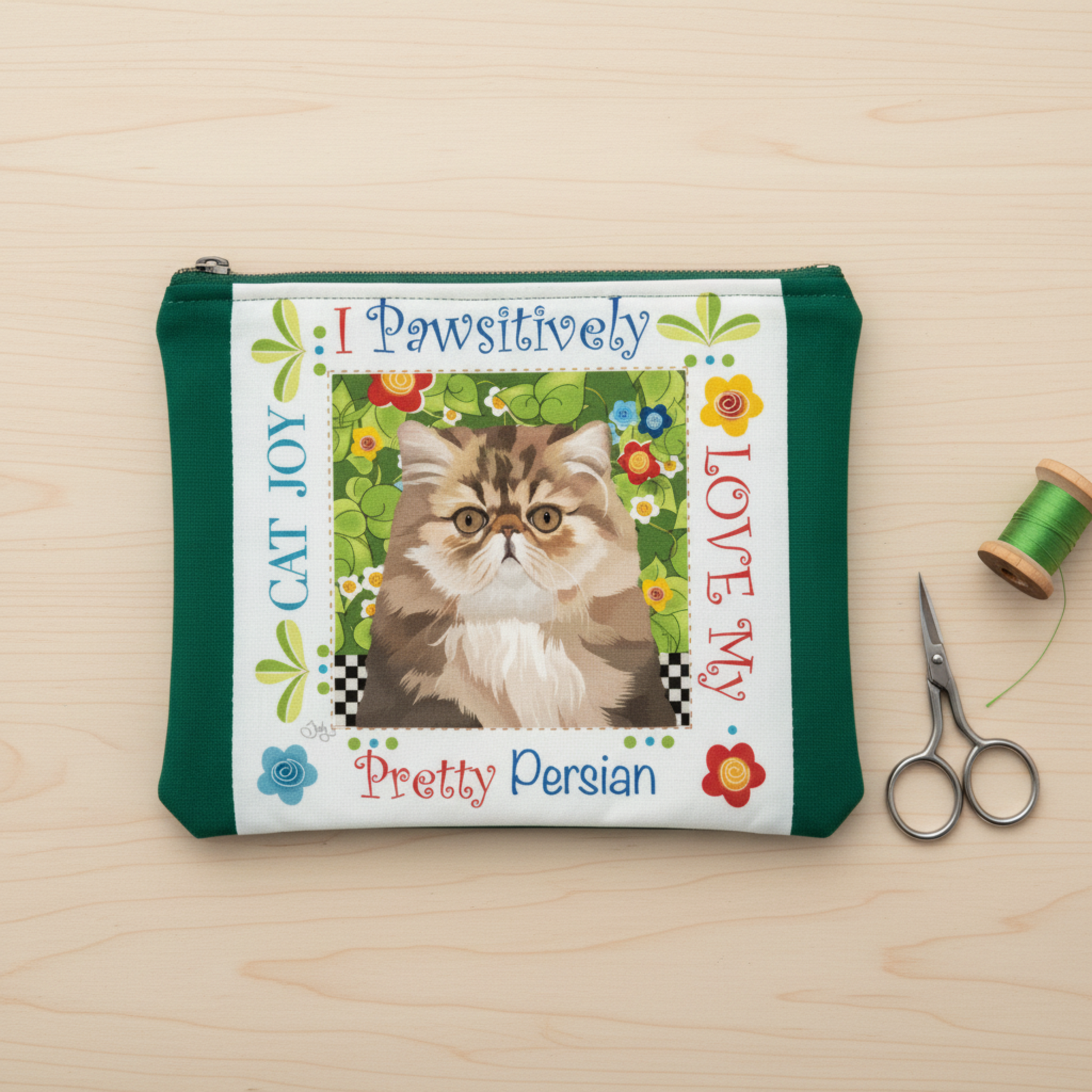Pretty Persian Cat Joy fabric art panel by Jody Houghton Designs sewn into a green zippered pouch – project idea for 6" novelty panel, shown with scissors and green thread spool on wood surface