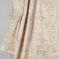 Expressions Batiks Breathe Ecru quilting cotton by Riley Blake Designs – Pinterest drape shot, soft gathered folds filling portrait frame showing natural drape and movement, warm cream and ecru tonal batik with pine needle and feathery frond motif in soft taupe and golden-beige, light grey background