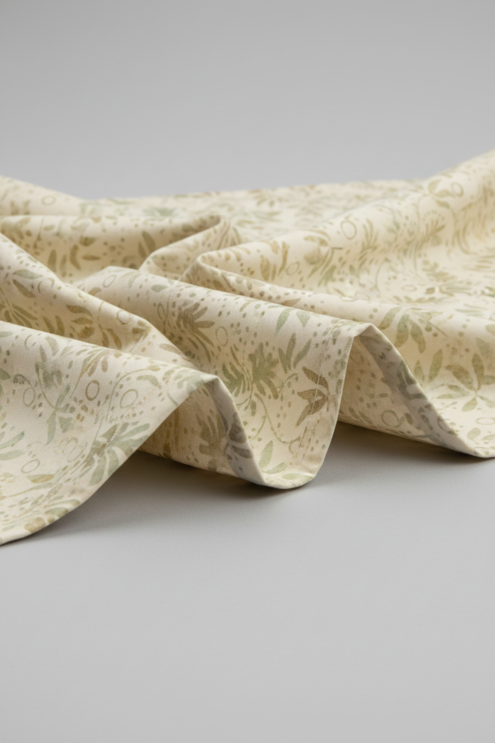 Expressions Batiks Breathe Laurel quilting cotton by Riley Blake Designs – Pinterest drape shot, soft accordion pleated folds filling portrait frame showing natural drape and movement, cream and ivory tonal batik with feathery fronds and dotted swirl outlines in soft sage green and warm taupe, light grey background