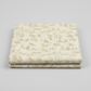 Expressions Batiks Breathe Laurel quilting cotton fabric by Riley Blake Designs – 2 neatly folded yards stacked on light grey background showing cream and ivory tonal batik with feathery fronds, dotted circular swirl outlines, and tiny leaf sprigs in soft sage green and warm taupe