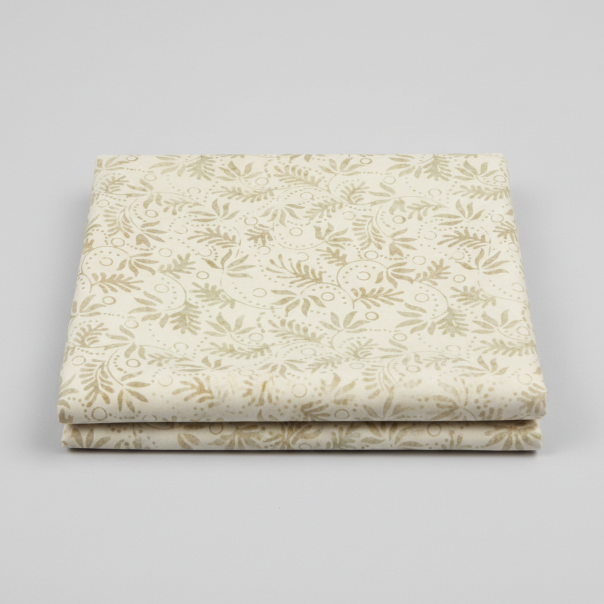 Expressions Batiks Breathe Laurel quilting cotton fabric by Riley Blake Designs – 2 neatly folded yards stacked on light grey background showing cream and ivory tonal batik with feathery fronds, dotted circular swirl outlines, and tiny leaf sprigs in soft sage green and warm taupe