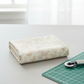 Expressions Batiks Breathe Flaxen by Riley Blake Designs – folded cream batik fabric on white surface beside green cutting mat and rotary cutter with soft natural window light, quilting workspace lifestyle shot