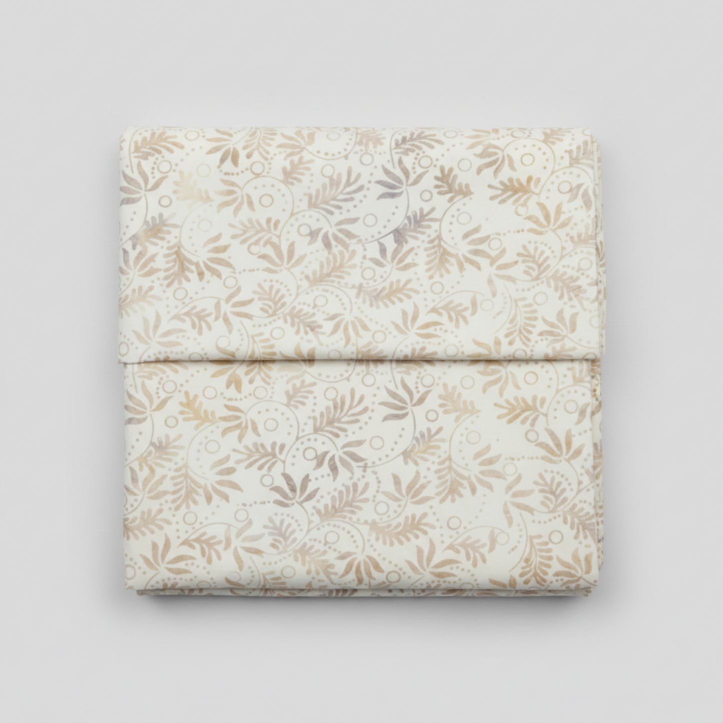 Expressions Batiks Breathe Flaxen by Riley Blake Designs – premium quilting cotton neatly folded on light grey background showing all-over swirling vine and feathery leaf batik pattern in soft warm gold, tan, and lavender-grey on cream background
