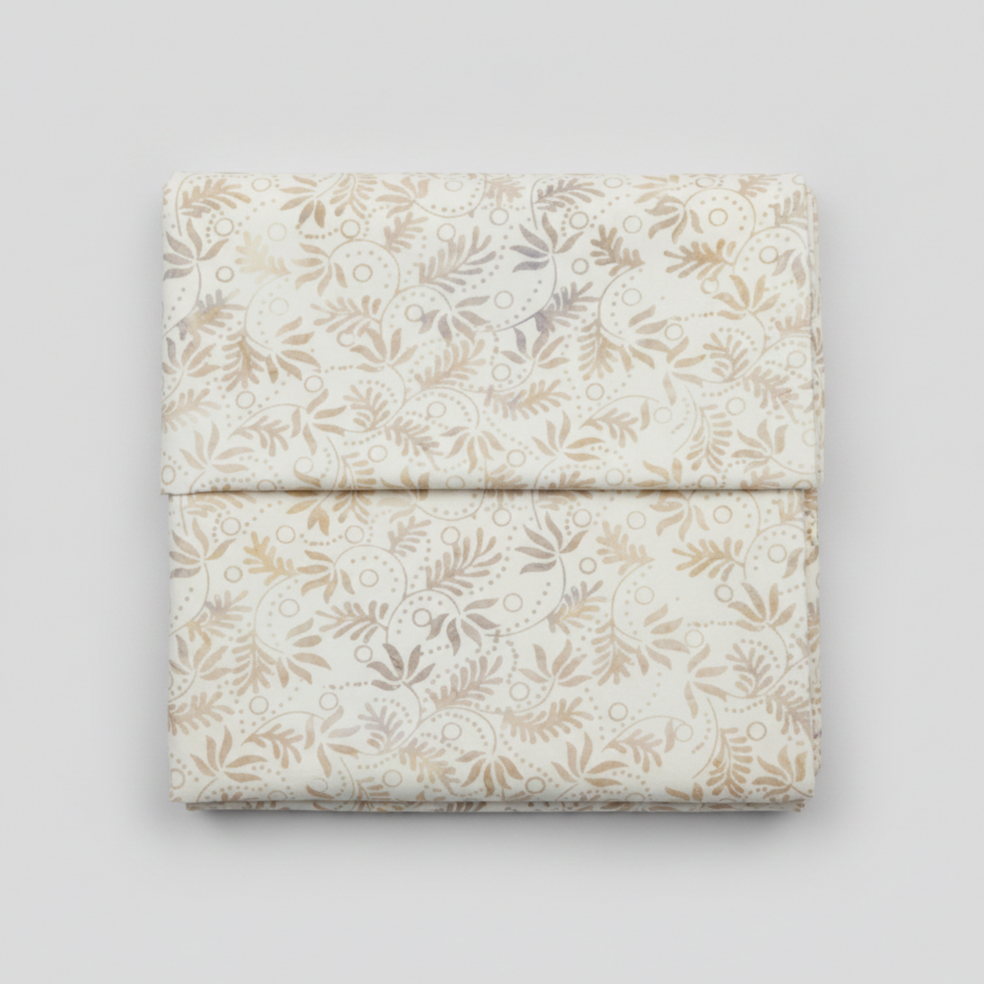 Expressions Batiks Breathe Flaxen by Riley Blake Designs – premium quilting cotton neatly folded on light grey background showing all-over swirling vine and feathery leaf batik pattern in soft warm gold, tan, and lavender-grey on cream background