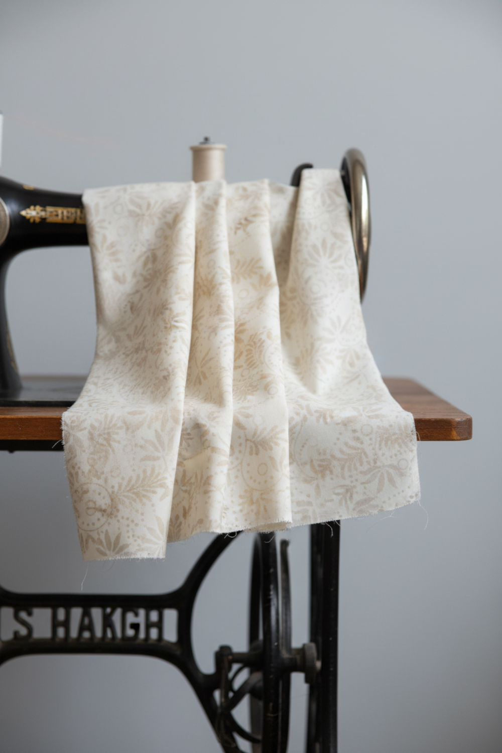 Expressions Batiks Breathe Flaxen by Riley Blake Designs – Pinterest drape shot showing cream batik fabric in soft pleated folds draped over antique black treadle sewing machine with warm wood surface on light grey background