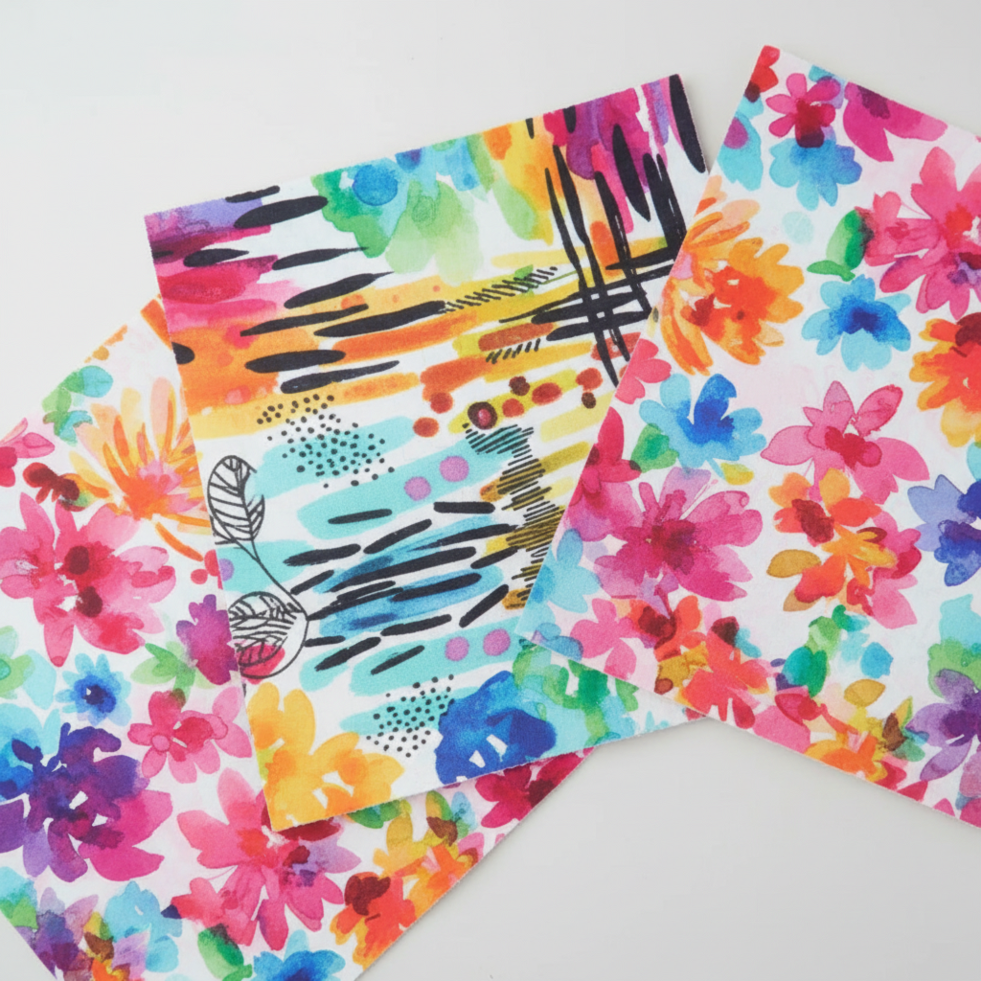 Close-up detail of Playgrounds charm pack 5" squares by Amarilys Henderson for Moda Fabrics – showing vibrant watercolor floral print with rainbow blooms alongside abstract mark-making print with black brushstrokes and botanical line art on multicolor background