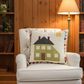 White armchair with a decorative pillow featuring a house design in a cozy room with wooden walls and bookshelves.