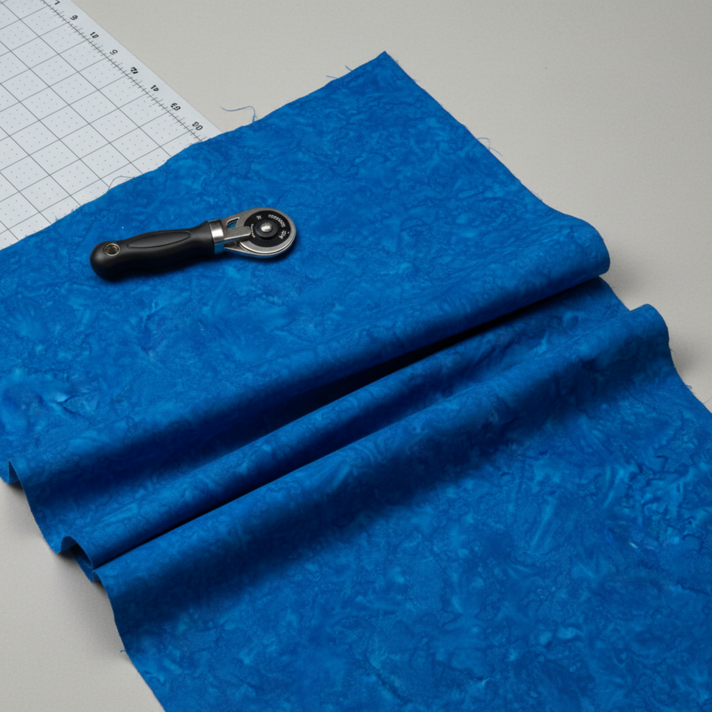 Expressions Batiks Hand-Dyed Imperial – fabric laying on table with rotary cutter and cutting mat visible, imperial blue hand-dyed batik
