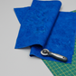 Expressions Batiks Hand-Dyed Cobalt quilting cotton with rotary cutter and edge of cutting mat on light grey background