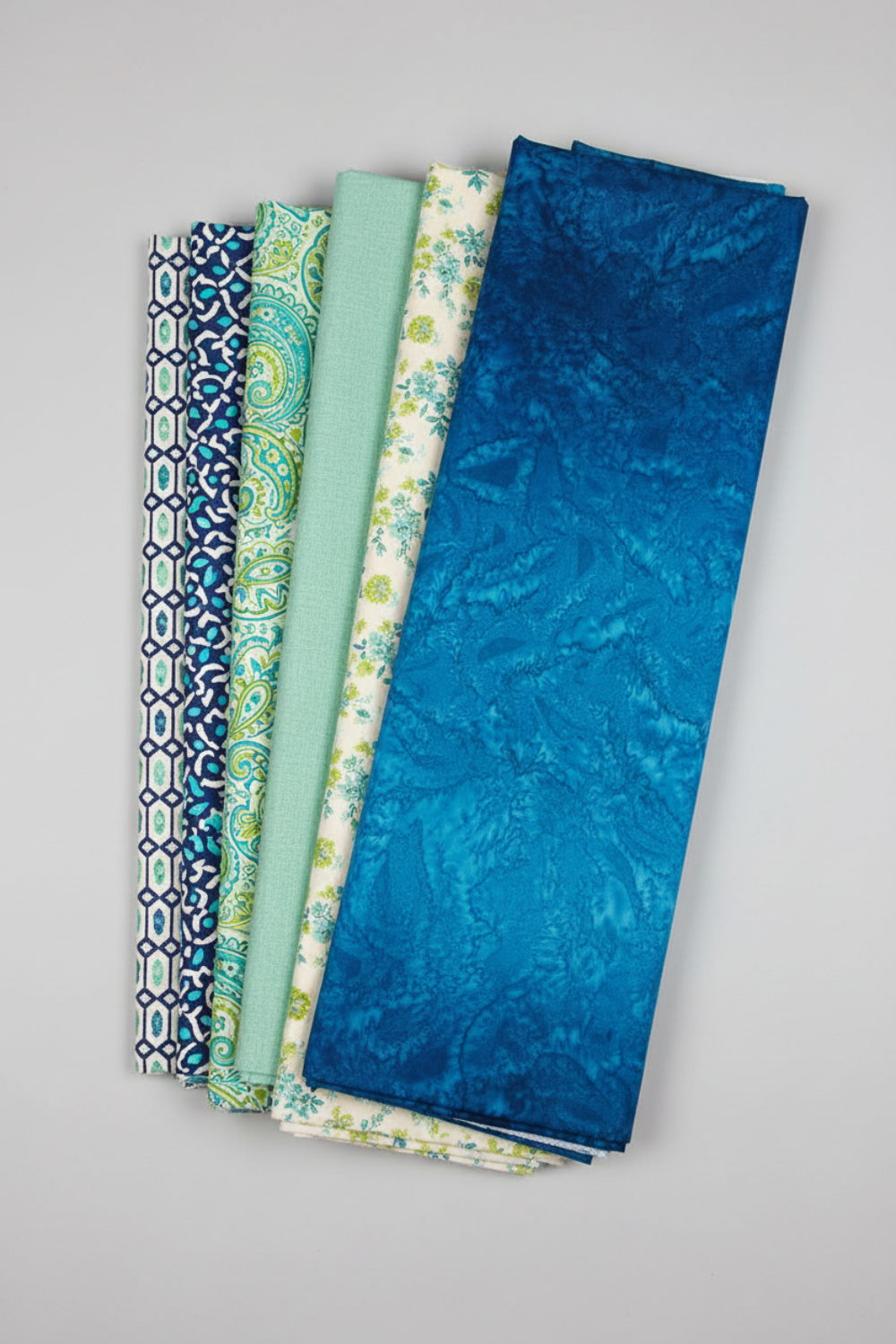 Six coordinating quilting fabrics including Hand-Dyed Ocean Blue fanned in complementary ocean and teal tones