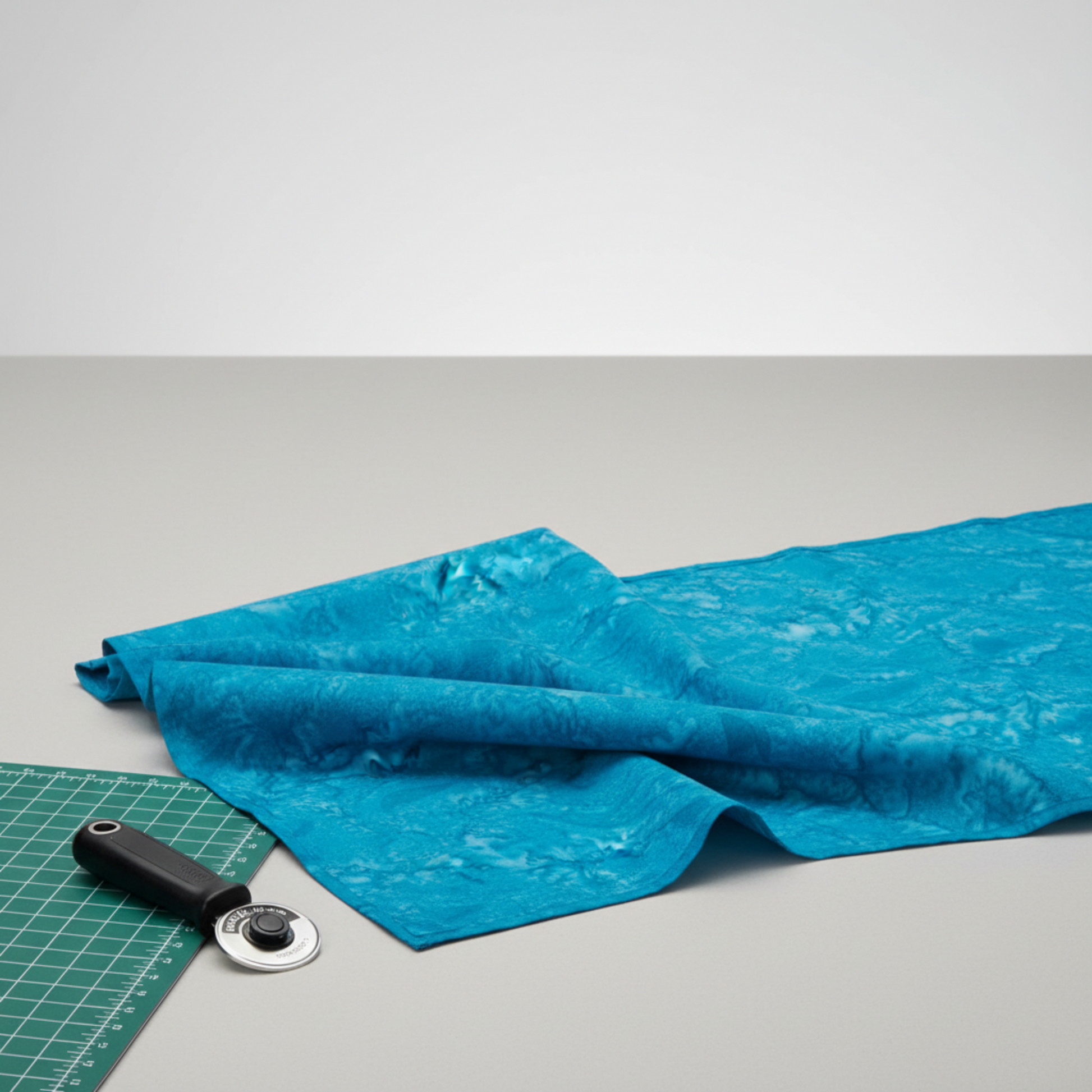 Expressions Batiks Hand-Dyes Hand-Dyed Ocean Blue quilting cotton fabric by Riley Blake Designs – ocean blue batik with soft drape on cutting mat alongside rotary cutter in quilting workspace