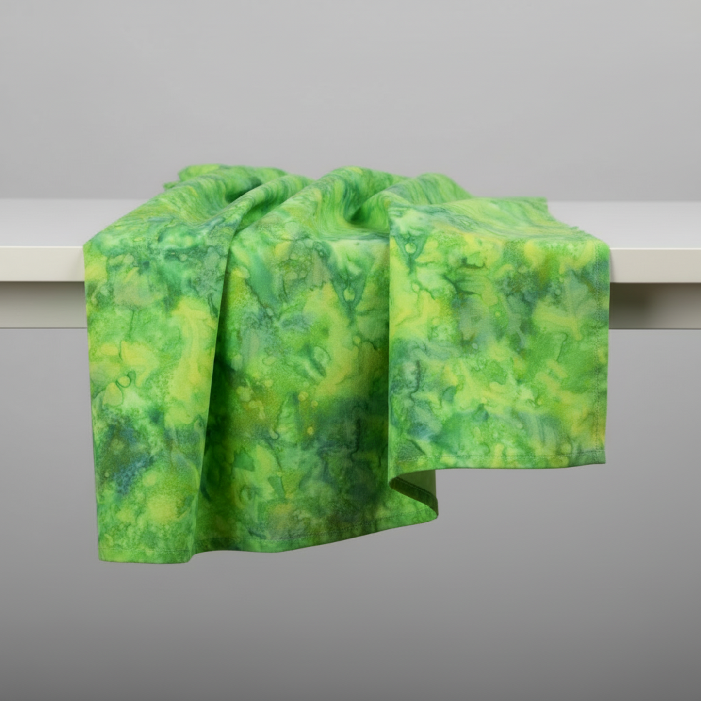 Expressions Batiks Hand-Dyed Shamrock quilting cotton fabric by Riley Blake Designs – bright shamrock green batik draped over table edge with natural soft folds on light grey background