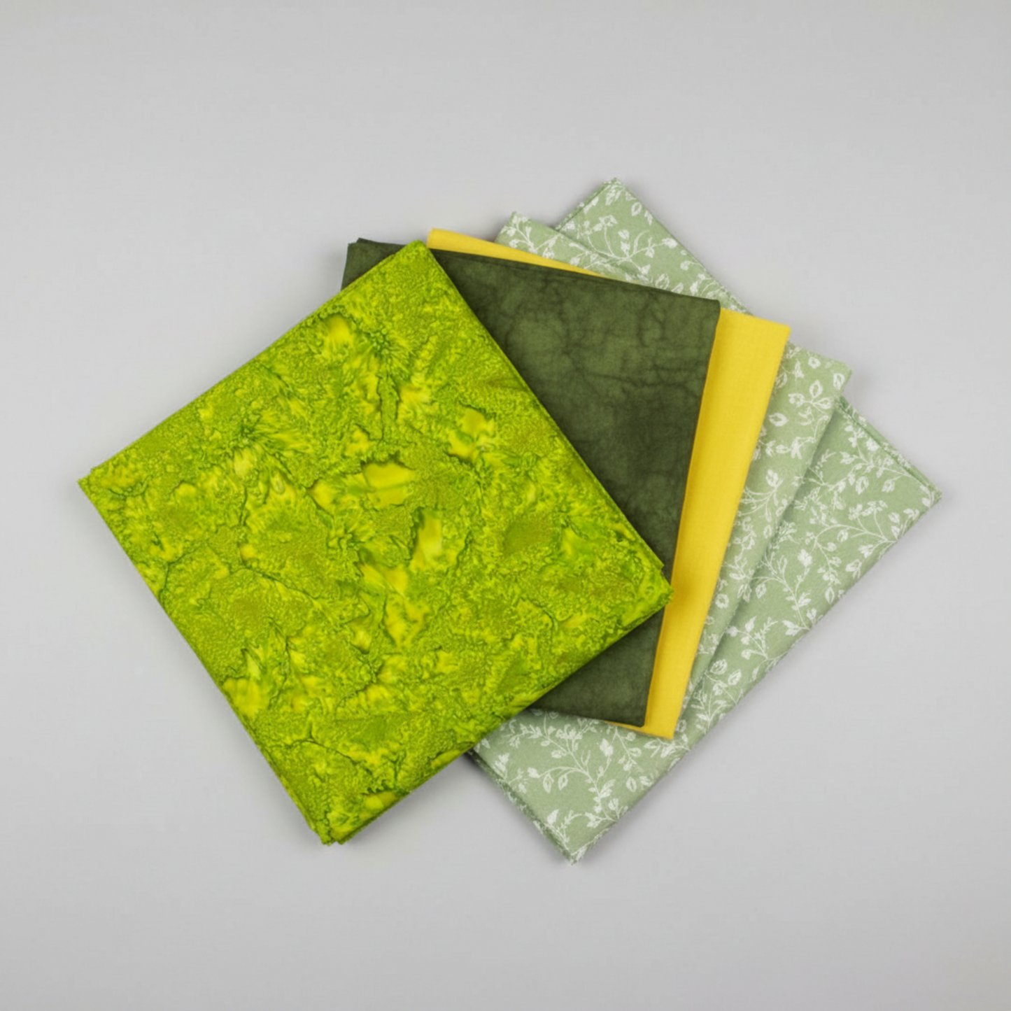 Expressions Batiks Hand-Dyes quilting cotton fabrics including Sap – 5 coordinating fabrics in complementary green and yellow tones slightly fanned on light grey background