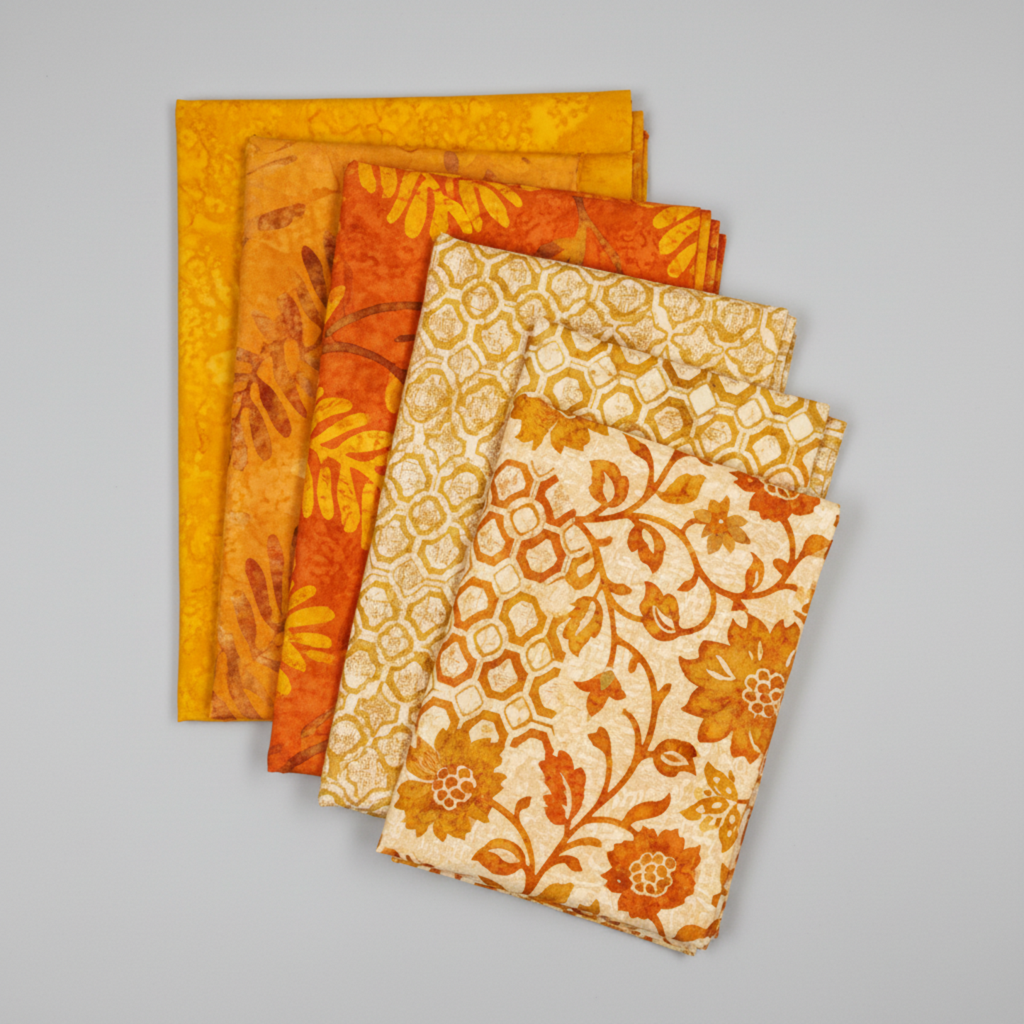 Expressions Batiks Hand-Dyes quilting cotton fabrics including Curry – 6 coordinating fabrics in complementary warm tones slightly fanned on light grey background