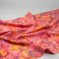 Expressions Batiks Hand-Dyed Bouquet quilting cotton fabric by Riley Blake Designs – vibrant golden orange, pink, magenta, and lavender hand-dyed batik in soft folds on flat surface showing texture and painterly tonal variation