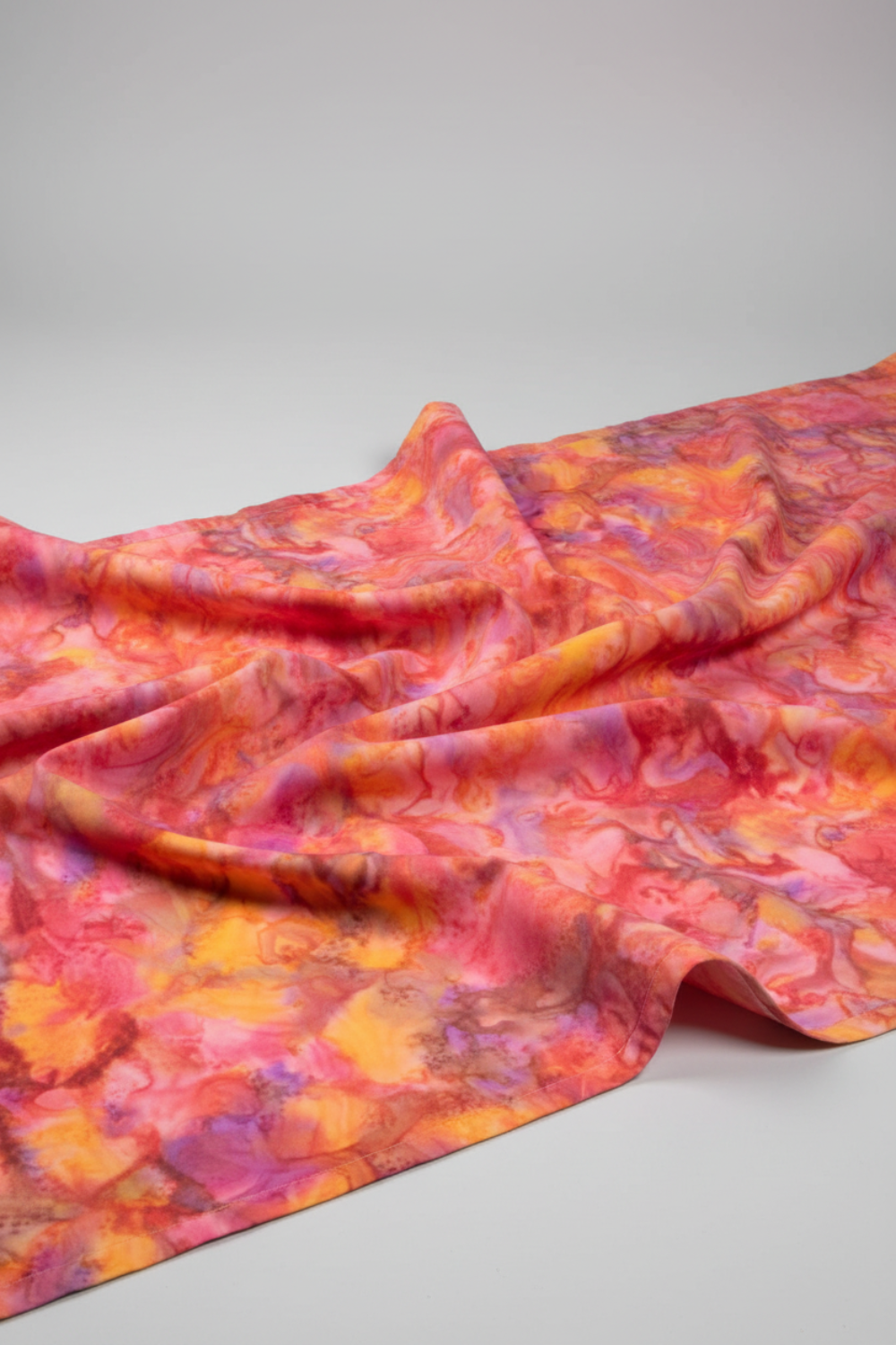 Expressions Batiks Hand-Dyed Bouquet quilting cotton fabric by Riley Blake Designs – vibrant golden orange, pink, magenta, and lavender hand-dyed batik in soft folds on flat surface showing texture and painterly tonal variation