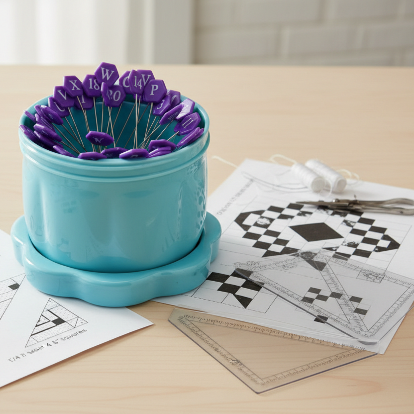 Alphabet quilting pins stored upright in magnetic pin cup next to quilt block pattern and rulers