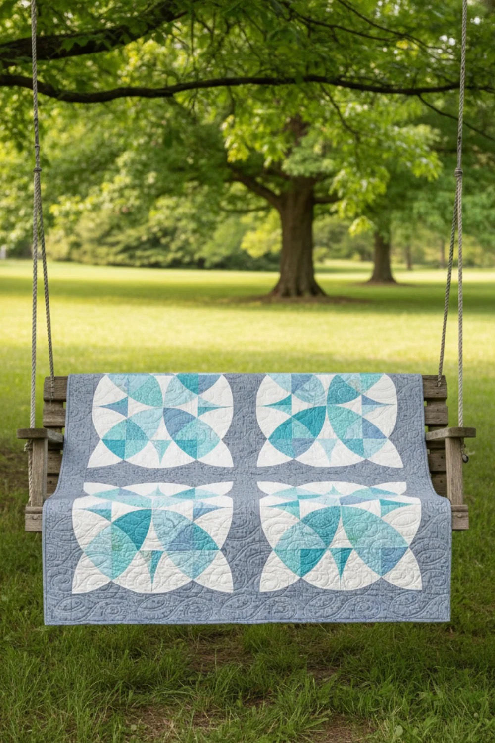 Country Revival quilt pattern by Sew Kind of Wonderful draped over a wooden porch swing in a lush green garden setting – curved piecing in soft aqua, teal, and white with pale blue-grey Spotted Mist fabric by Zen Chic for Moda Fabrics used in the blocks – available at IraRobi Quilts