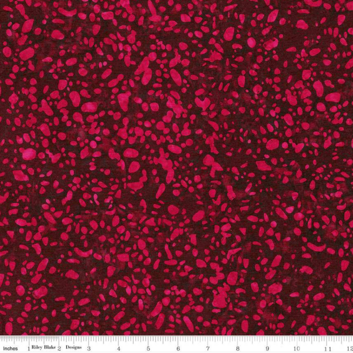 Terrazzo Mahogany batik fabric by Riley Blake Designs, showing raspberry-magenta terrazzo speckles on a deep burgundy ground with an inch ruler showing print scale