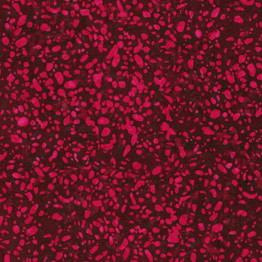 Close-up of Terrazzo Mahogany batik fabric by Riley Blake Designs, with raspberry-magenta pebble-shaped speckles on a mottled deep burgundy ground