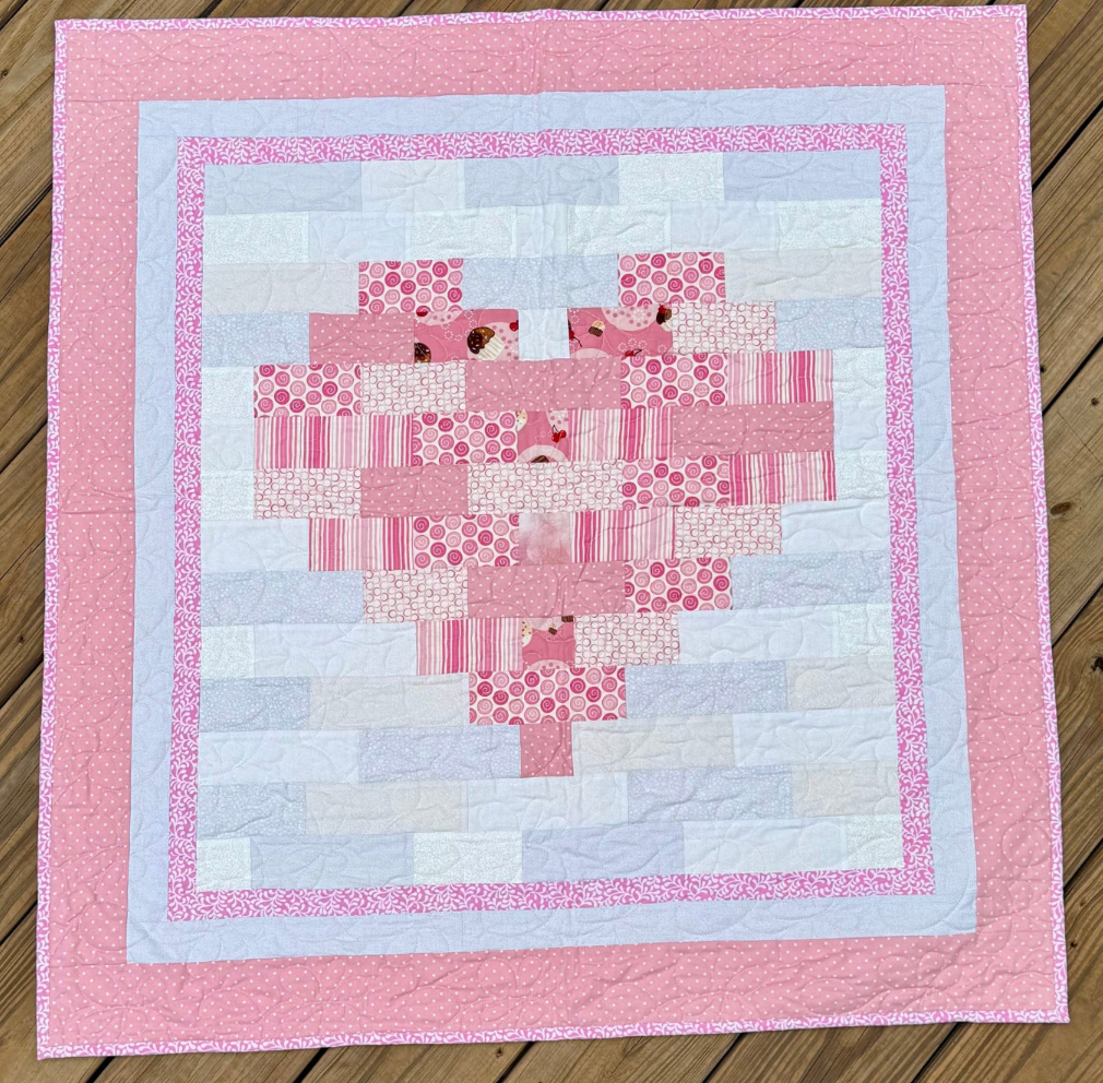 Quilt with pink heart pattern on a wooden surface