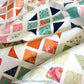 Hopscotch Happy quilt close-up flat lay showing colorful half square triangle blocks in orange, pink, teal, navy and floral prints on white background with scallop machine quilting by Robin Pickens
