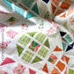 Hopscotch Happy quilt close-up flat lay showing colorful half square triangle blocks in teal, green, orange, pink and floral prints on white background with scallop machine quilting by Robin Pickens