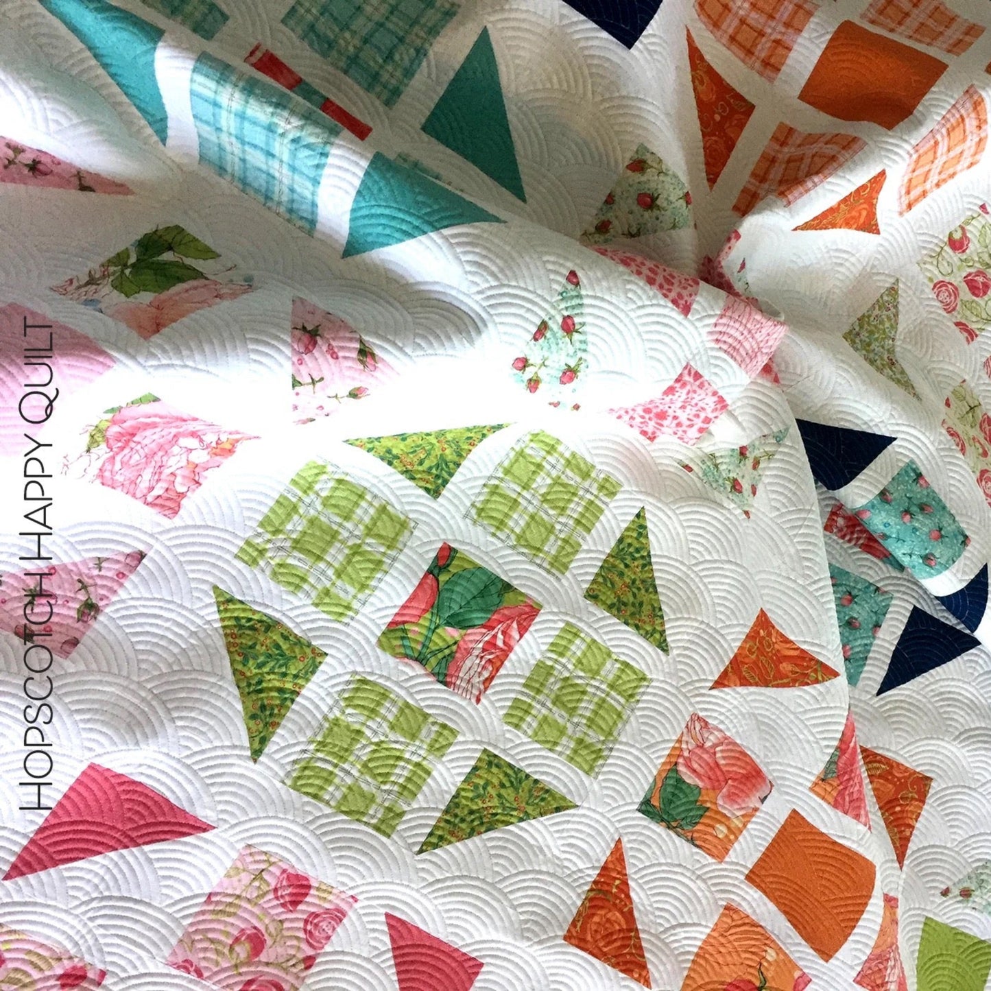 Hopscotch Happy quilt close-up flat lay showing colorful half square triangle blocks in teal, green, orange, pink and floral prints on white background with scallop machine quilting by Robin Pickens