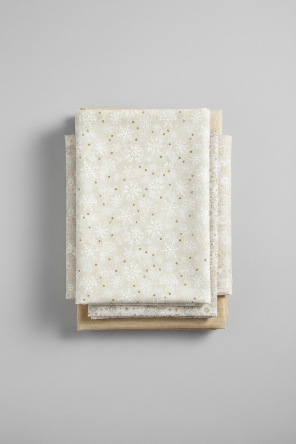 Winter Solstice II Cream Snowflakes Metallic quilting cotton styled in folded stack – lifestyle shot for quilters