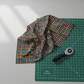 On the Go Plaid Multi quilting cotton fabric from the On The Go collection, multicolor plaid pattern draped on green cutting mat with rotary cutter for scale.