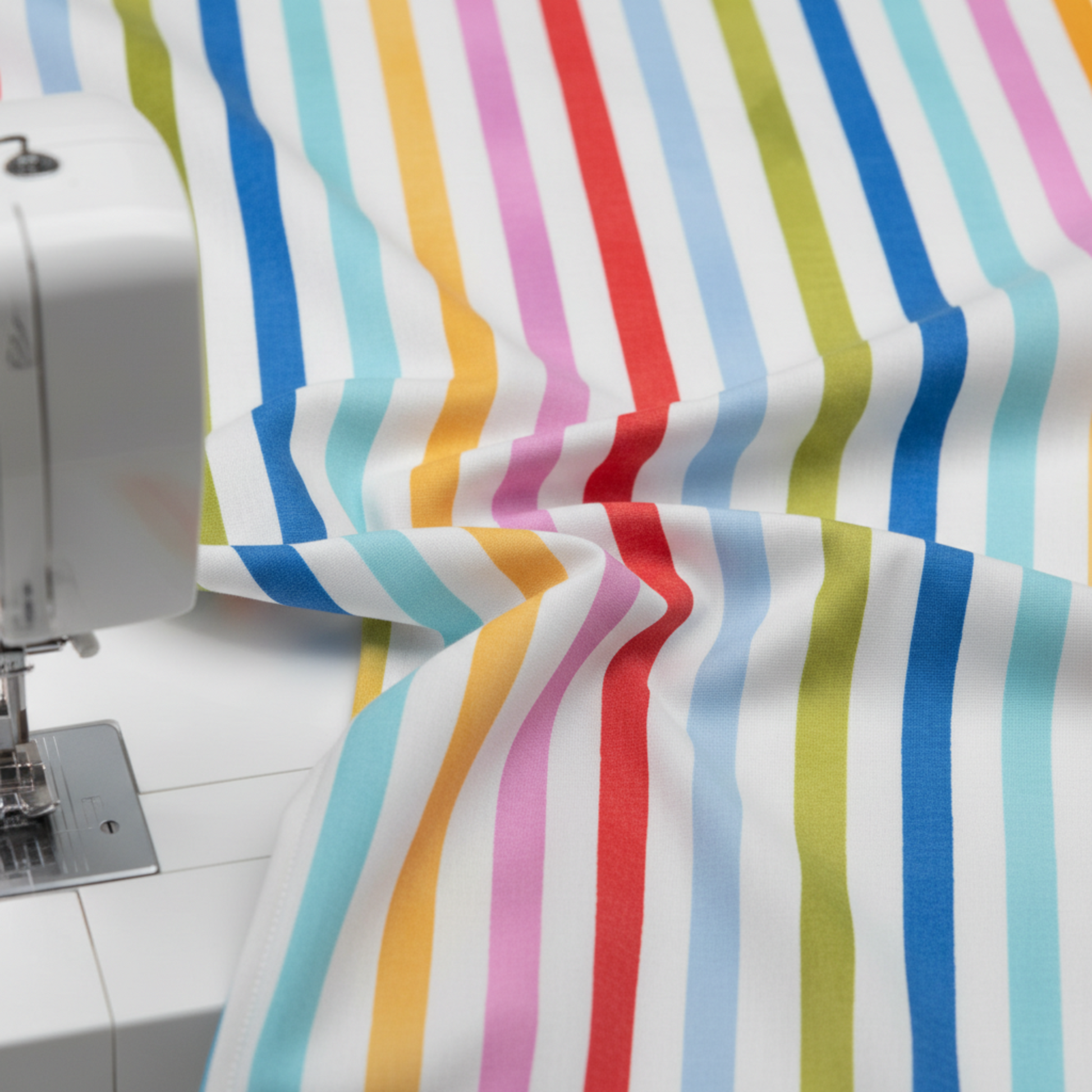 On the Go Stripes Multi fabric flowing beside sewing machine, bright striped quilting cotton for modern patchwork projects.