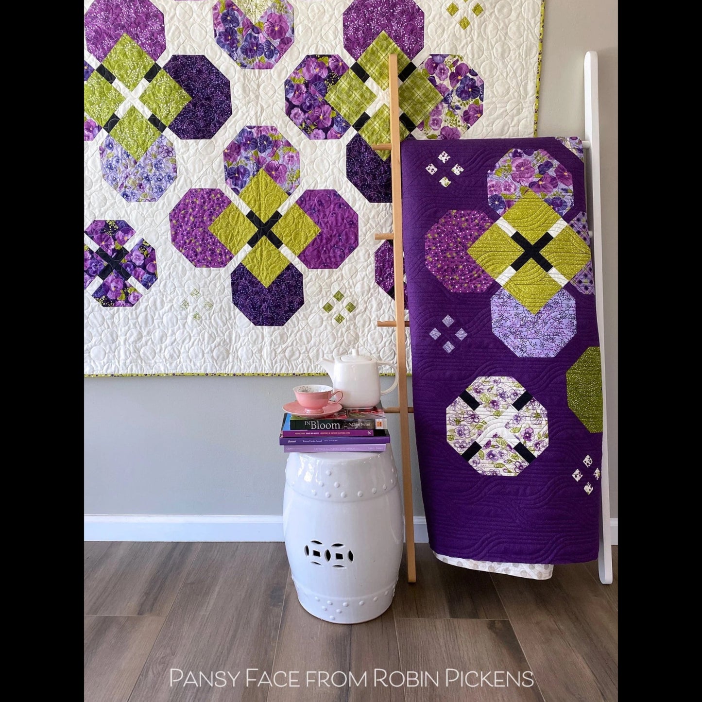 Pansy Face quilt pattern lifestyle photo — full lap quilt displayed on wall with purple queen quilt on white ladder and garden stool by Robin Pickens