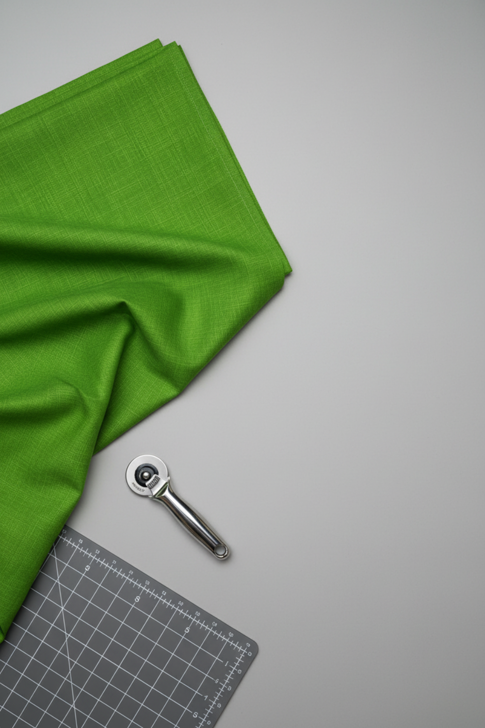 Interwoven Green quilting cotton lifestyle photo showing draped fabric on table surface with cutting mat and rotary cutter