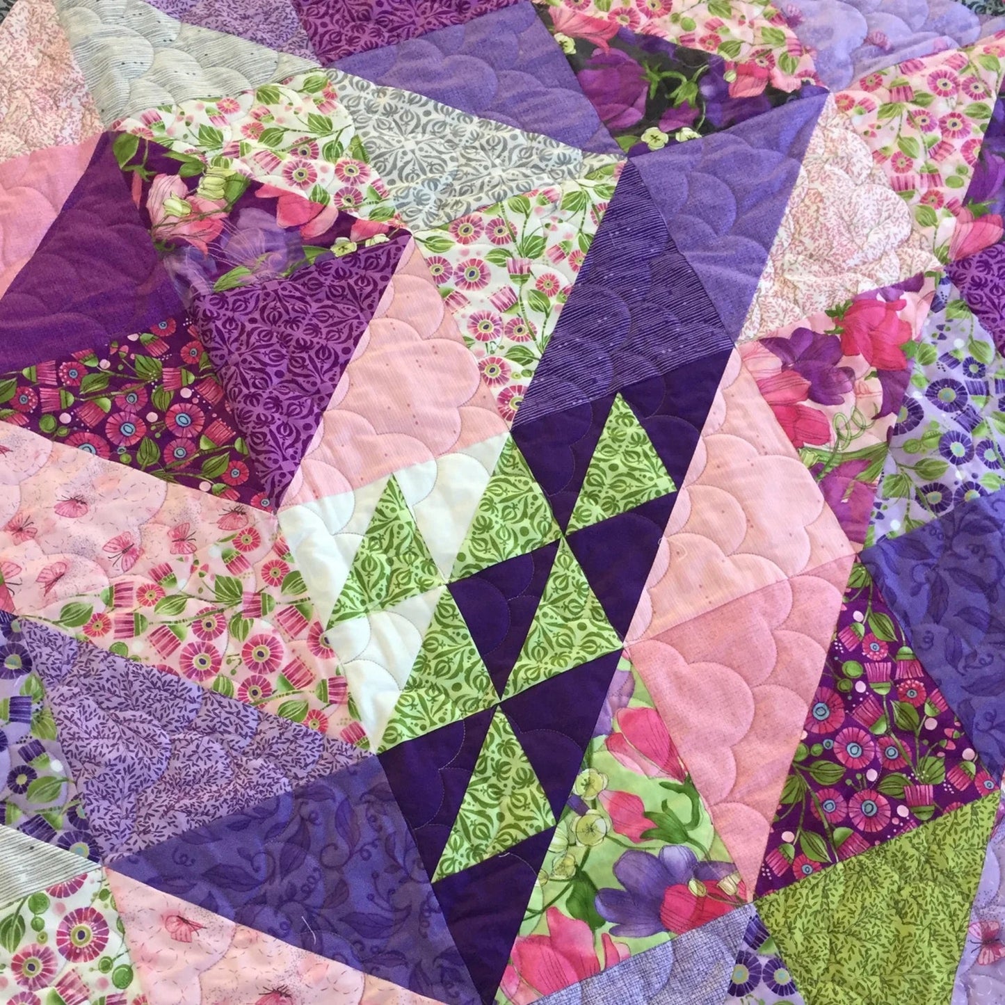 Faceted quilt close-up showing purple, pink and chartreuse green half square triangle blocks with crystal-like radiating design and floral Sweet Pea fabrics