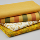 Expressions Batiks Hand-Dyed Yellow Orange Multi III quilting cotton by Riley Blake Designs – Pinterest coordination stack of 4 warm-toned quilting fabrics including yellow-orange multicolor batik, mustard yellow solid, olive and terracotta stripe, and cream leaf print on light grey background