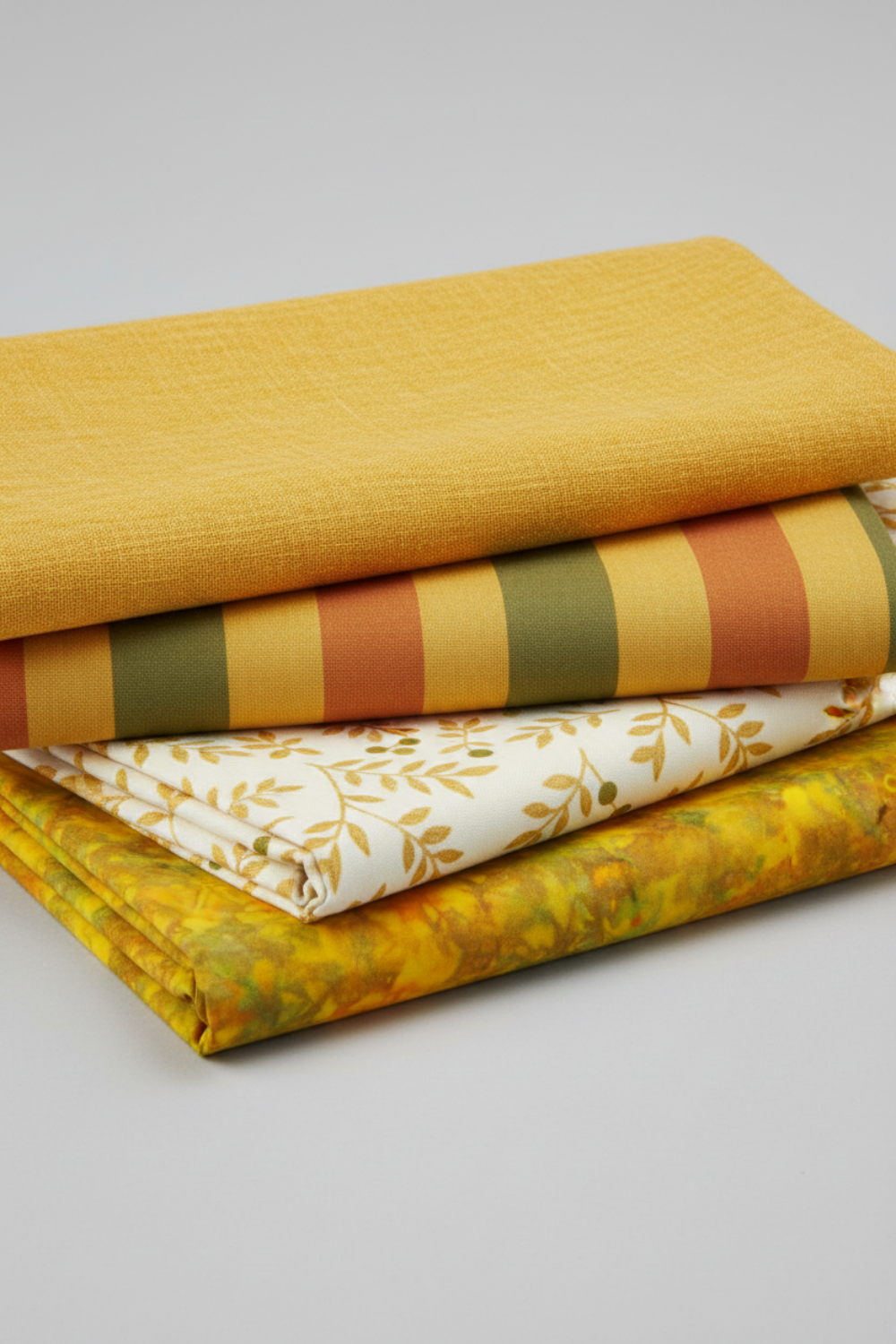 Expressions Batiks Hand-Dyed Yellow Orange Multi III quilting cotton by Riley Blake Designs – Pinterest coordination stack of 4 warm-toned quilting fabrics including yellow-orange multicolor batik, mustard yellow solid, olive and terracotta stripe, and cream leaf print on light grey background