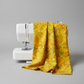 Expressions Batiks Hand-Dyed Yellow Orange Multi III quilting cotton fabric by Riley Blake Designs – vivid multicolor hand-dyed batik draped over white sewing machine showing natural drape and movement, golden yellow, orange, and olive green palette, light grey background