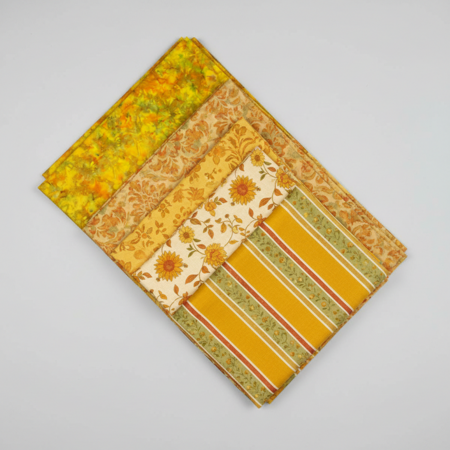 Expressions Batiks Hand-Dyed Yellow Orange MultiIII quilting cotton by Riley Blake Designs – coordination stack of 5 fanned warm-toned quilting fabrics including yellow-orange multicolor batik, golden floral tonal, cream sunflower print, mustard yellow solid, and olive green stripe on light grey background